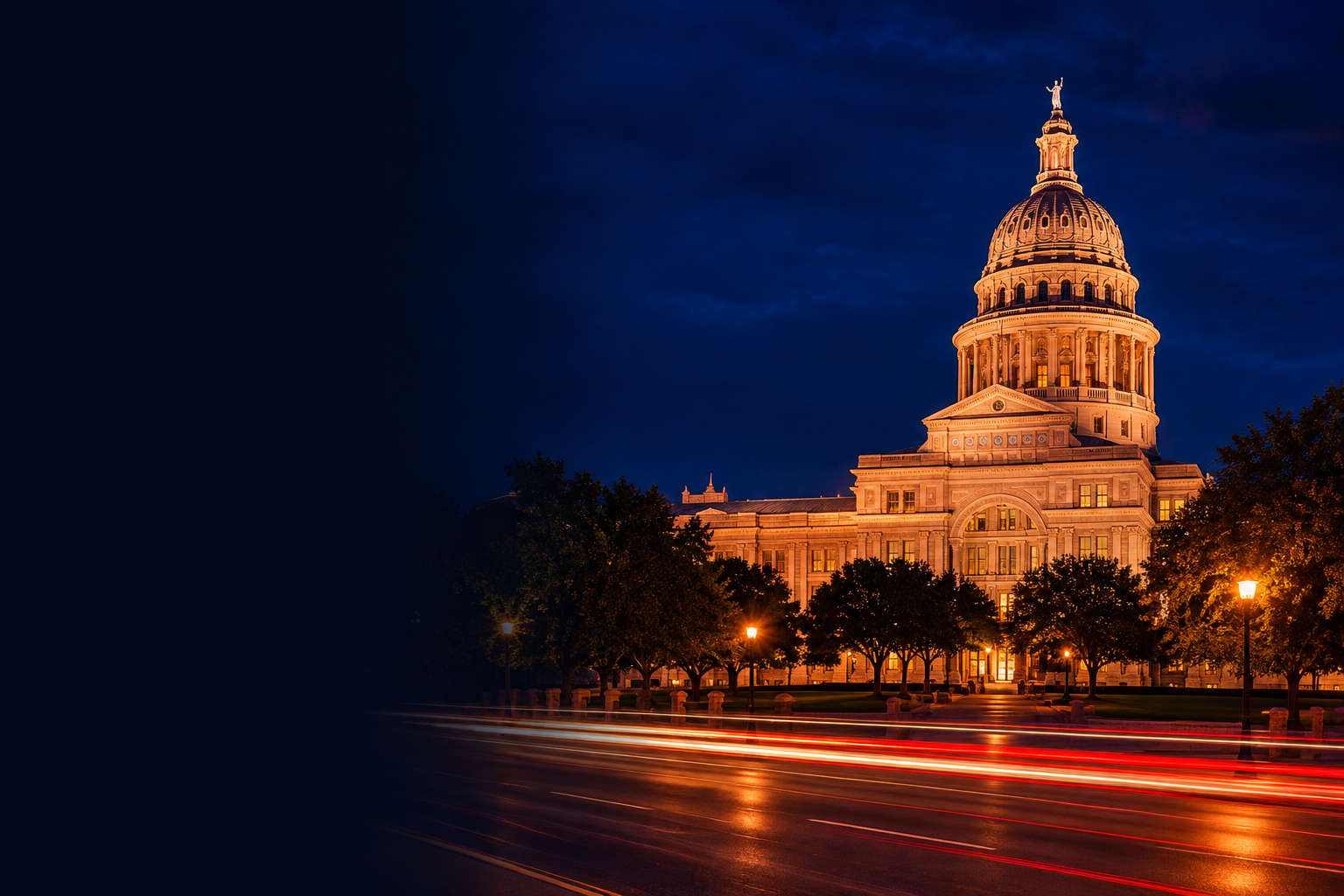 A domed granite capitol lit amber at night, with red and white car light trails on the avenue in front.